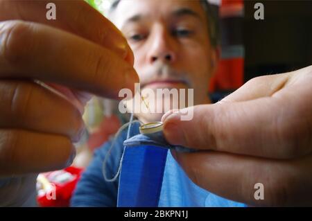 Tailor man with needle and thread in the hand. Handmade work. Manual sewing on the shirt button. Home handcraft. Stock Photo