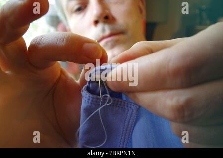 Tailor man with needle and thread in the hand. Handmade work. Manual sewing on the shirt button. Home handcraft. Stock Photo