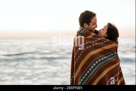 Loving young couple wrapped in a blanket at the beach Stock Photo