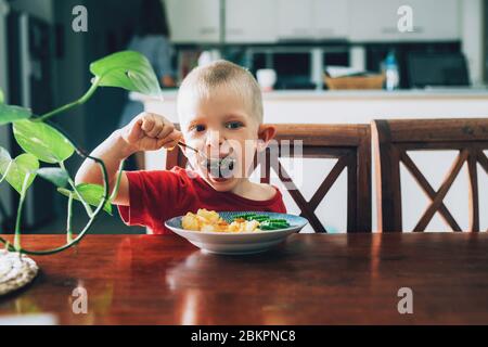 Cute child, preschool boy, eating veggies for lunch in the dining room. Stock Photo