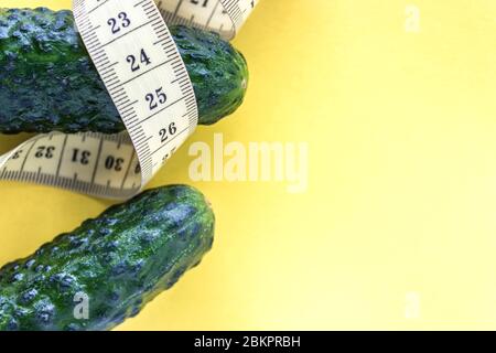 Fresh green cucumbers and yellow measuring tape on a yellow background, place for text. Healthy eating concept Stock Photo