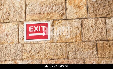 Red exit sign on sandstone textured wall 16:9 background Stock Photo