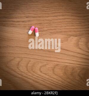 2 pink and white ibuprofen capsules sitting on a wooden table Stock Photo