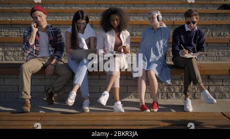 Multiethnic Group of Friends sitting outside, everyone is doing Stock Photo