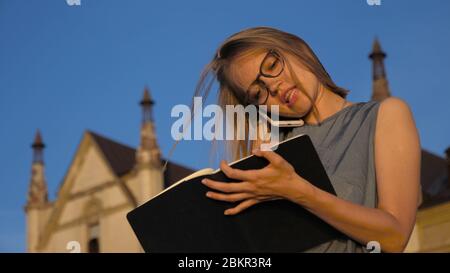 Business woman talking on the phone and makes notes outside. Stock Photo