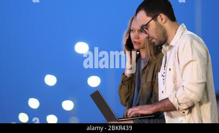 Two coworkers using laptop and young businesswoman making call. Stock Photo