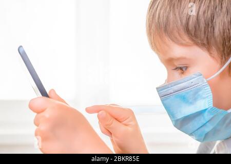 Boy studying online at home using tablet. Kid in medical mask studying online. Studying during quarantine. E learning concept. Home school. Pandemic, Stock Photo
