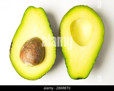 Two avocado halves opposite ways up with the stone left in one half on a white background Stock Photo