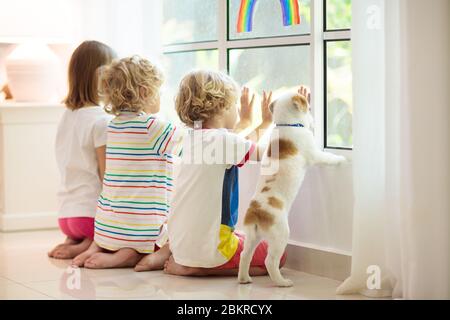 Coronavirus quarantine. Stay home. Kids sitting at window. Children drawing rainbow sign of hope. Boy and girl during corona virus lockdown. Child and Stock Photo