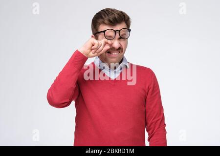 Tired caucasian man in rd sweatersuffer from eyesight problems or blurry vision rubbing his eye. Exhausted stressed European male massage eyes having Stock Photo