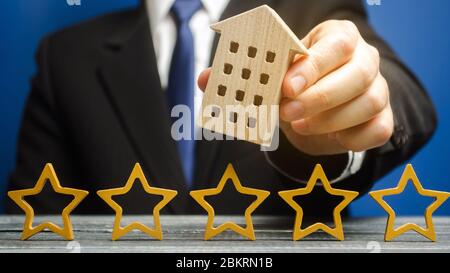 Five stars and a wooden house in the hands of a businessman. The concept of the best housing, luxury apartments VIP class. The best service. Feedback. Stock Photo