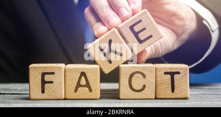 A man puts wooden blocks with the words Fact and fake. Concept of news and false information. Yellow press. Stock Photo