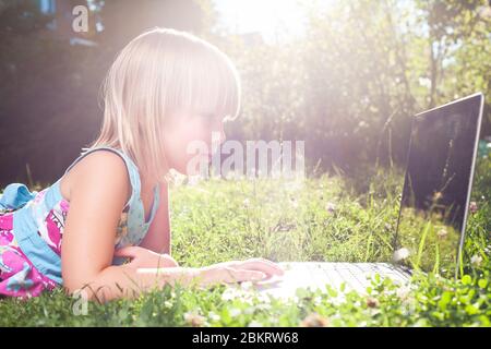 Little girl using laptop computer in a garden backyard. Child studying homework during online lesson at home being on self-isolation or quarantine Stock Photo