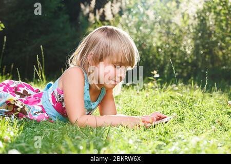 Little girl using a tablet computer in a garden backyard. Child studying homework during online lesson at home being on self-isolation or quarantine Stock Photo