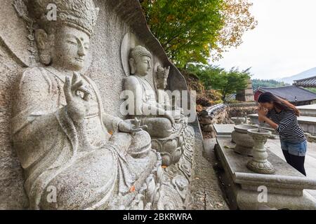 South Korea, South Gyeongsang Province, Ssanggyesa temple, young Asian woman praying in front of a Buddha sculpture Stock Photo