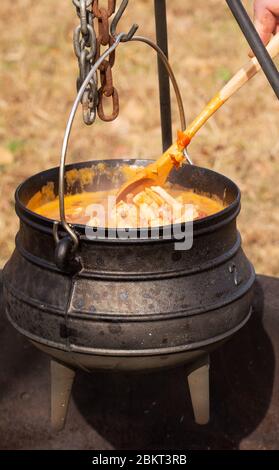Stew cooking in a potjie cast iron pot over open fire outdoors Stock Photo