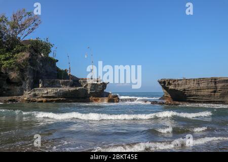 The tide floods the coast at a temple built on a rock in the sea. Hindu temple Tanah Lot on Bali, Indonesia. Surf shatters on rock cliffs. Azure blue Stock Photo