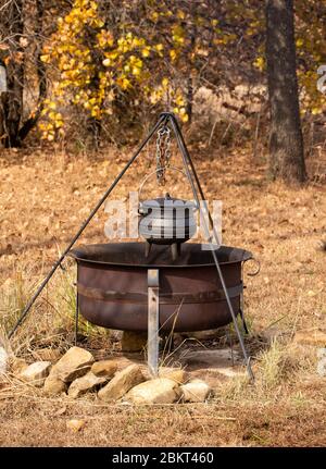 Stew cooking in a cast iron potjie suspended over open fire in a fire pit outdoors; with fall color background Stock Photo