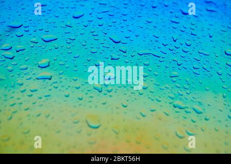 Water drops on the chameleon holographic surface. Beautiful colorful background with shallow depth of field. Blue and yellow gradient. Stock Photo