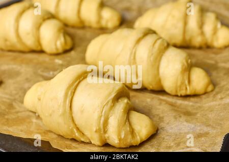 Producing of classic croissants from rolled layered dough. at home. Raw classic crescent rolls on a baking paper. Traditional french pastry Stock Photo