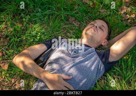 drunk man with a bottle of alcohol under his arm resting on a green field Stock Photo