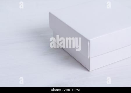 Closed white gift box with a lid on isolated wooden background. Crop image, side view, square box. Elegant eco-friendly mockup. Isolated box with Stock Photo