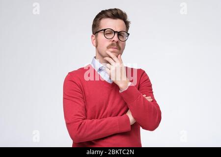 Casual man in red sweater and glasses thinking with a hand in his chin on white isolated background Stock Photo