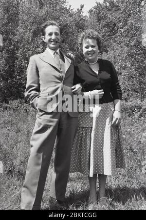 1950s, historical, happy adult couple, mid-late thirties in age, posing outside for a picture, the suited gentleman smoking a pipe, common among male adults in this era, England, UK. Stock Photo