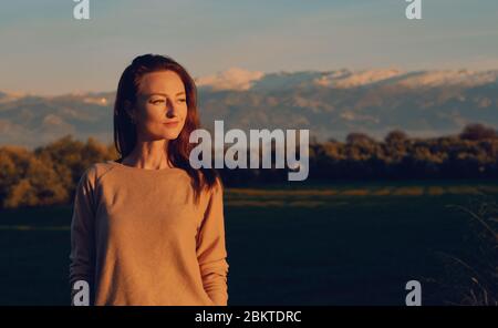 Young woman pose against Sierra Nevada mountain ridge background. Traveller girl standing outdoors during sundown looking in distance. Tourism concept Stock Photo