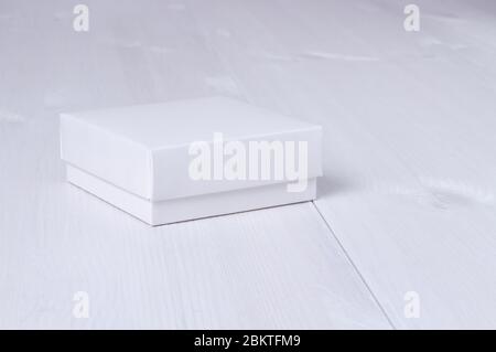 Closed white gift box with a lid on isolated wooden background. Side view, square box. Elegant eco-friendly mockup. Isolated box with cover on white Stock Photo