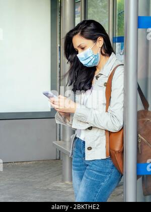 Woman standing in the bus stop. She is wearing a protective mask for the prevention of a virus. Coronavirus concept.