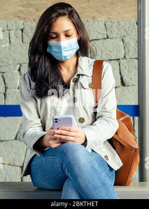 Woman sitting in the bus stop. She is wearing a protective mask for the prevention of a virus. Coronavirus concept.