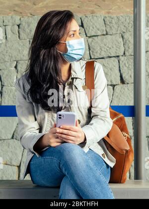 Woman sitting in the bus stop. She is wearing a protective mask for the prevention of a virus. Coronavirus concept.