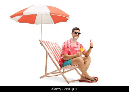 Man with sunglasses drinking cocktail and sitting under umbrella on a deckchair isolated on white background Stock Photo