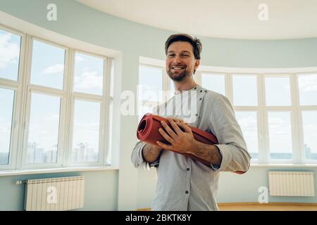 Portrait of a man holding yoga mat. Smiling attractive male holding yoga mat and looking at camera. Stock Photo