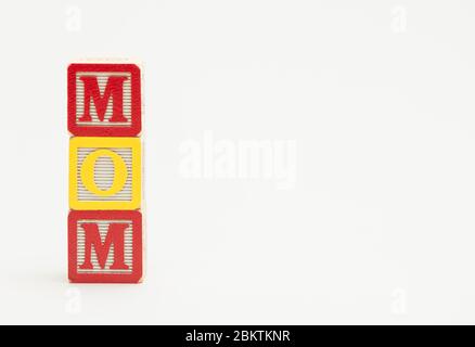 Three small wooden toy blocks spell the word mom in colorful letters on a white background. Stock Photo