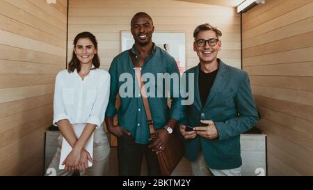 Group of diverse business professionals. Three multi-ethnic business people standing together in office looking at camera and smiling. Stock Photo