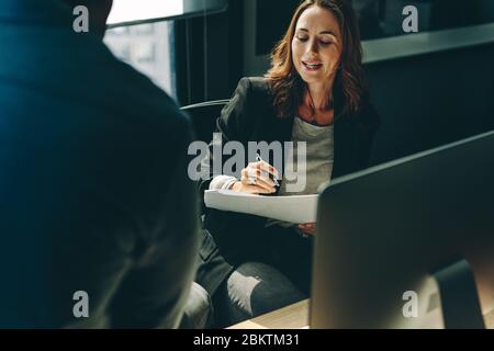 businesswoman looking at a document and talking with male colleague in office. business colleagues discussing over a report in office. Stock Photo