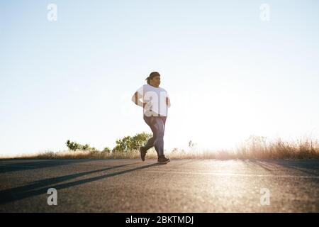 Plus size woman running in morning. Overweight woman doing morning workout on the road. Stock Photo