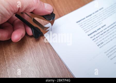 11 Close up of human hand using a staple remover to remove a staple from sheets of paper on a wooden desk in a commercial office Stock Photo
