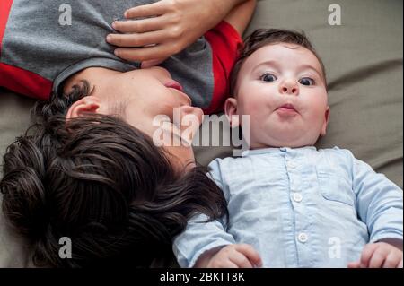 Daily life. High angle view of a happy boy lying in bed with his baby brother. Stock Photo