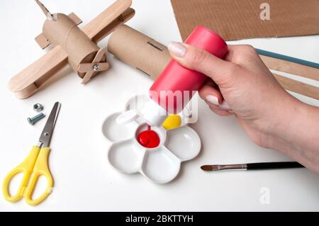 How to make airplane. Hand made toy,zero waste from toilet paper roll and popsicle sticks. For kids and parents. Step 5,put red paint. Stock Photo