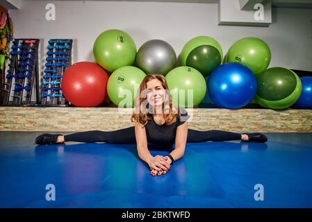 Slim athletic young woman in sportwear does sport stretching exercises in fitness club gym. Stock Photo