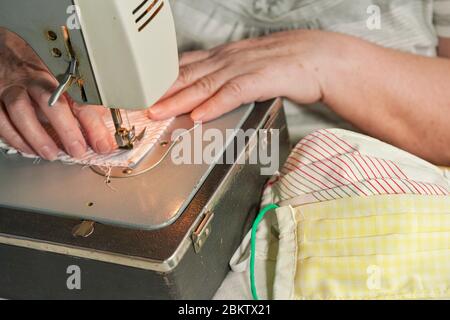Elderly senior woman working on old sewing machine - making home made face mask against coronavirus spreading, closeup detail to finished pile of prot Stock Photo