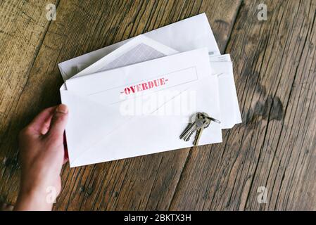Hands of a woman hold an letter with that reads Overdue in an envelope - Keys - Table - Late Payment Stock Photo