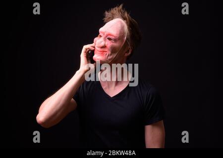 Portrait of young man with horror mask thinking while talking on the phone Stock Photo