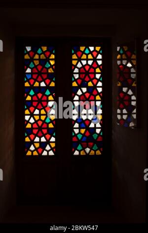 A door made of stained-glass colored glass. The pattern is reflected on the glass. The photo is dark and looks intimidating. The pattern on the stained-glass window is made of many pentagons. Stock Photo