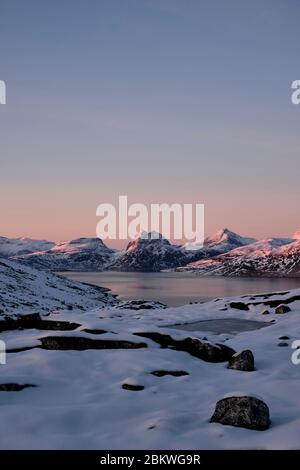 vivid colorful sunset over water with snow covered mountain range in the background. Stock Photo