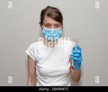 Young nurse with mask on her face holding test tube with glove in her hand in laboratory Stock Photo