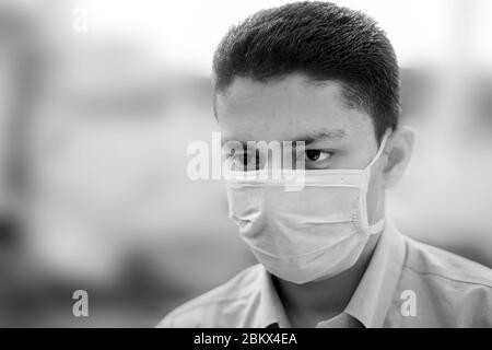 Portrait shot of a young man in blue colored shirt and wearing a surgical mask or a procedure mask with blurred background. Stock Photo